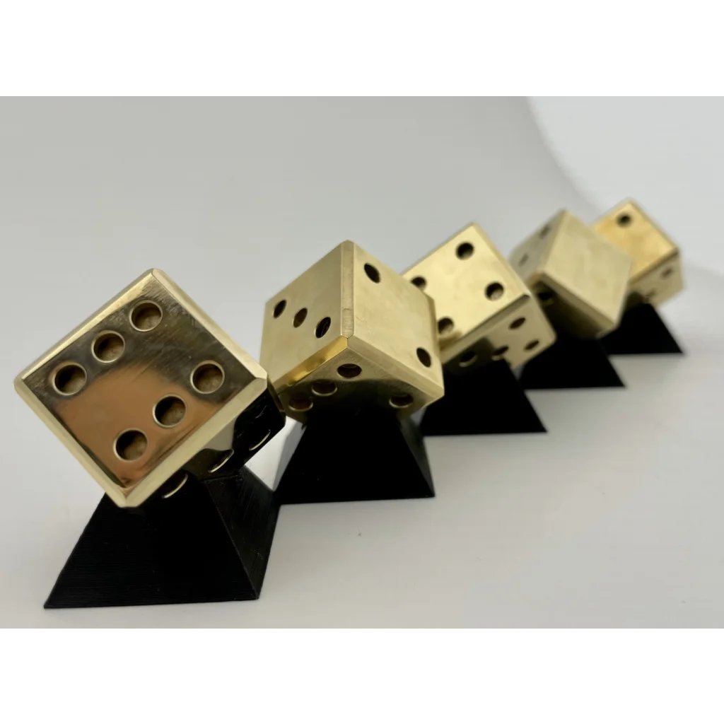 A row of UNLIMIT3D FIVE - set of 5 dices in brass, copper or stainless steel sitting on top of each other.